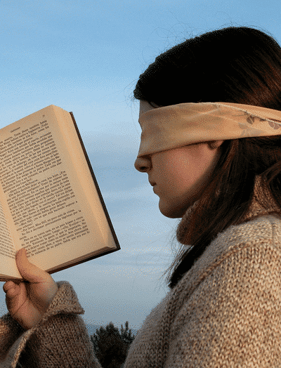 Woman trying to read book whilst blindfolded